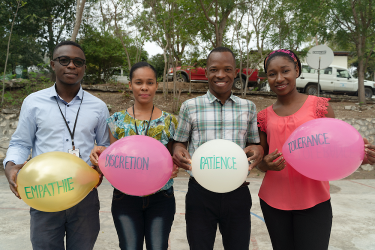 Four social workers, two men and two women, stand next to each other and smile at the camera. Each person holds a balloon with writing on it. The balloons says empathy, discretion, patience, and tolerance in French.